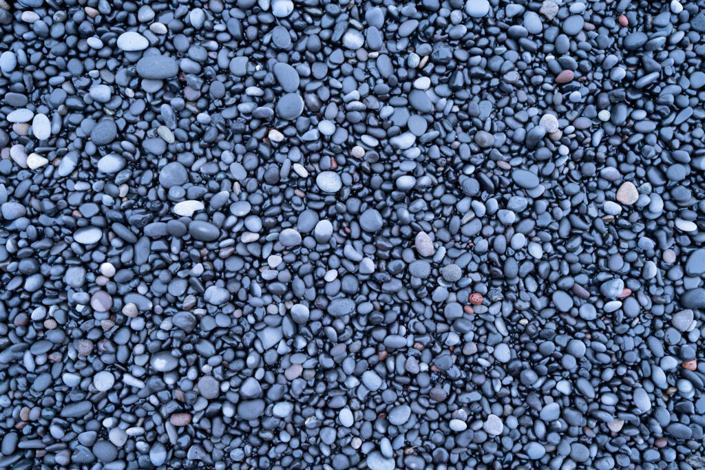 Close-up of smooth gray and black river rock aggregate stones covering the ground, showing a mix of small rounded pebbles in varying sizes and shades.